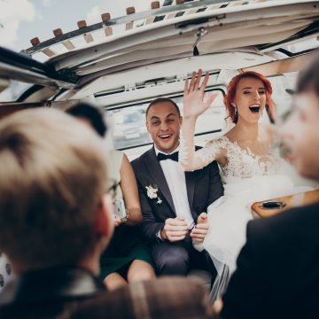 stylish happy bride and groom having fun and dancing inside of retro car smiling. emotional moment, space for text. luxury wedding newlyweds party with bridesmaids and groomsmen